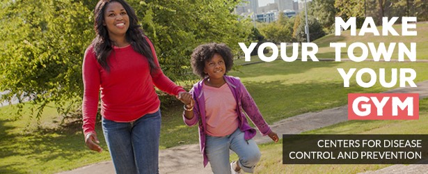 A color photo of an African American mom and young daughter walking on a park path.